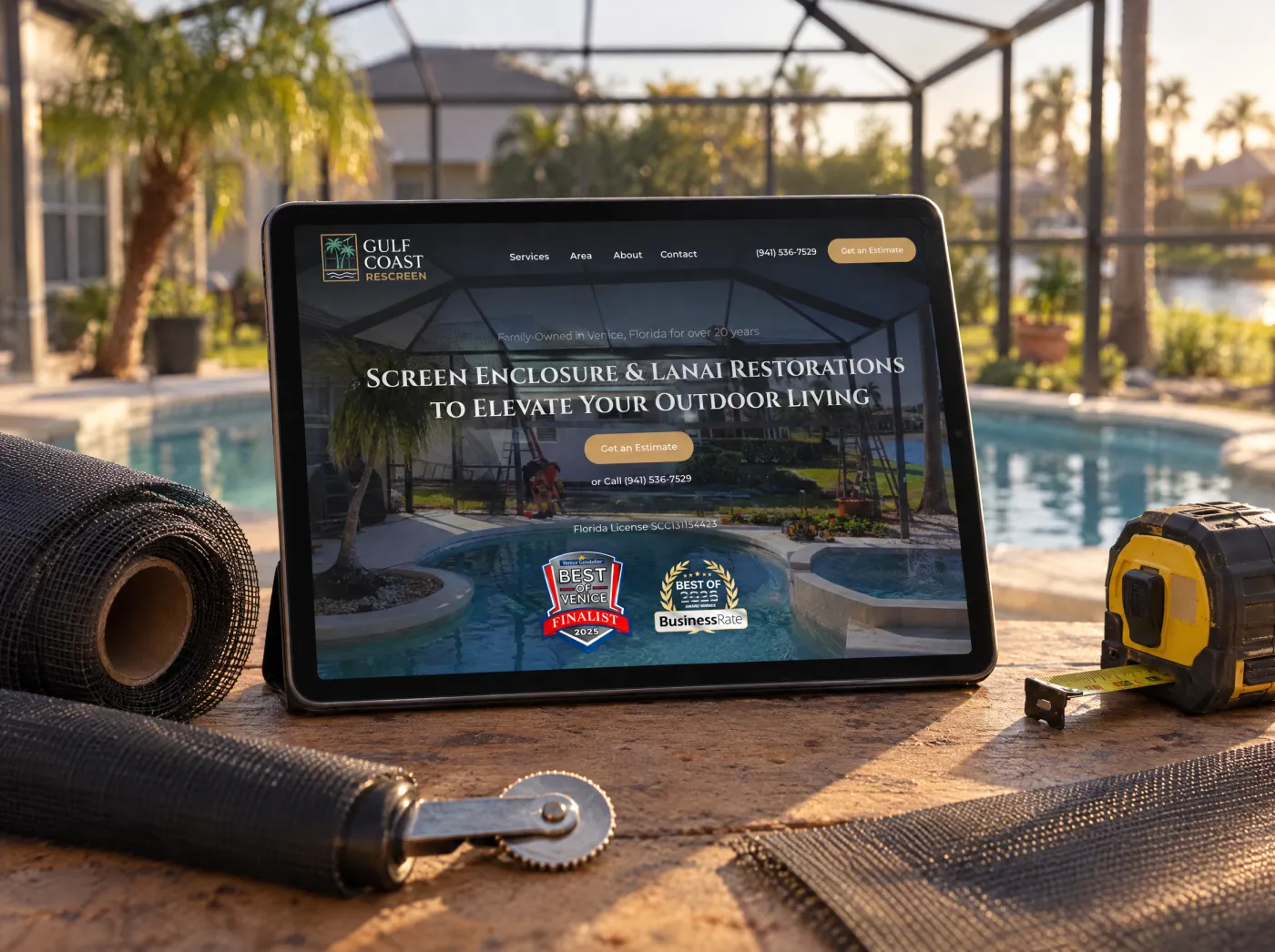 The Gulf Coast Rescreen website on a tablet on a workbench under a pool cage, beside rolls of screen mesh and a spline roller.
